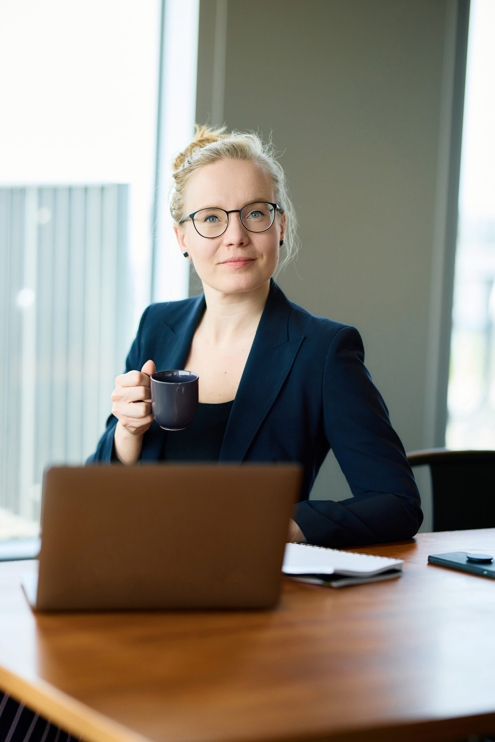 Mareike Walther upper-body business portrait looking at camera while holding a coffee cup, professional and approachable