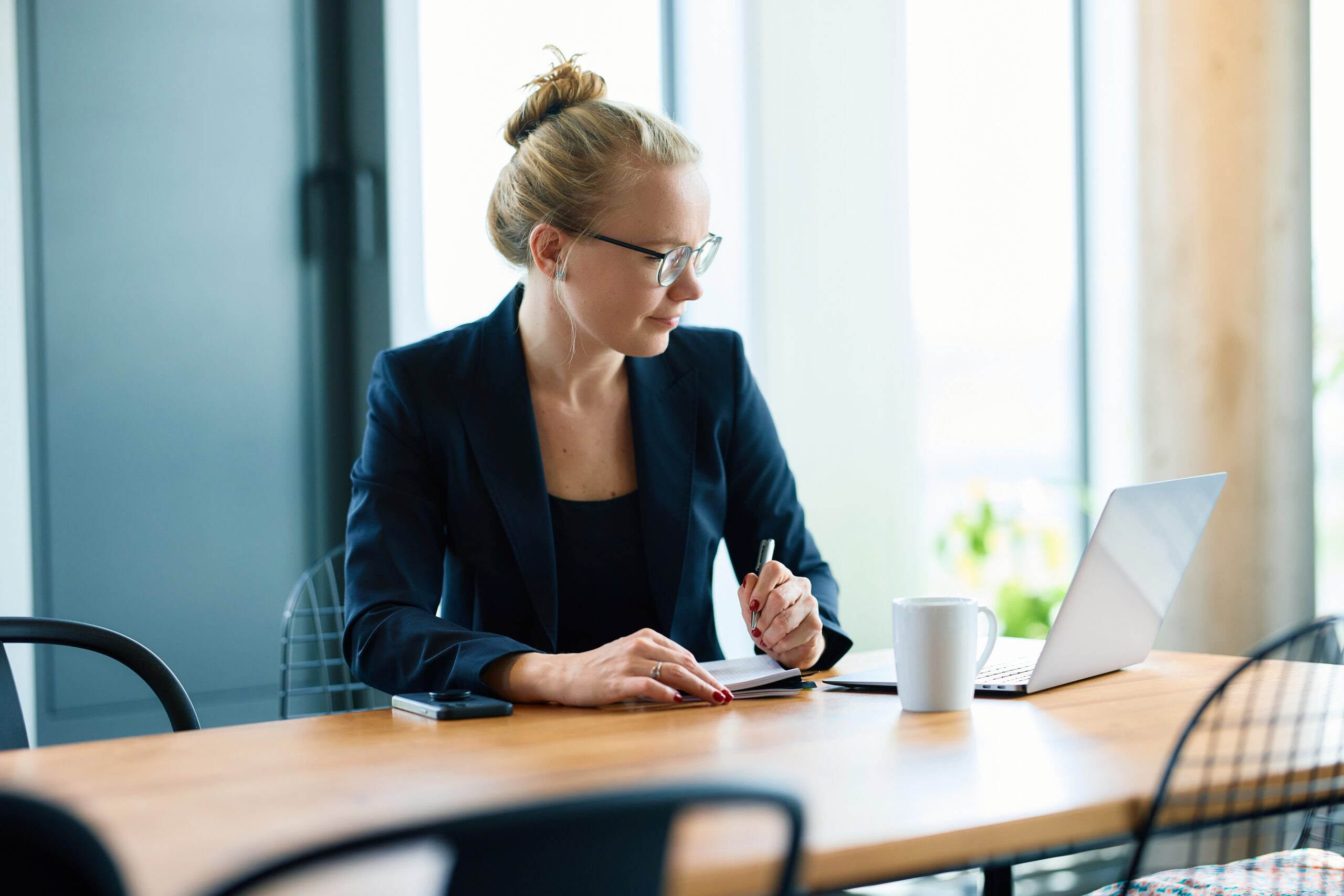 Mareike Walther upper-body portrait looking thoughtfully at computer screen while taking notes, professional setting